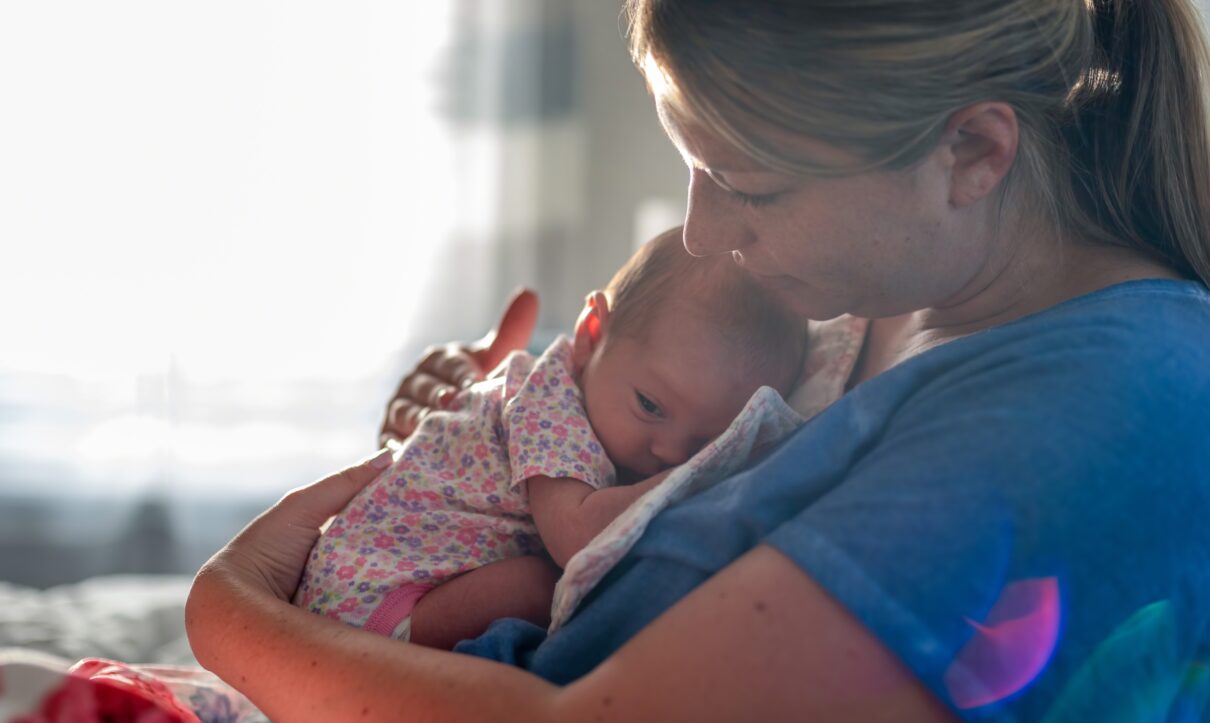 Young woman holding newborn daughter in natural light